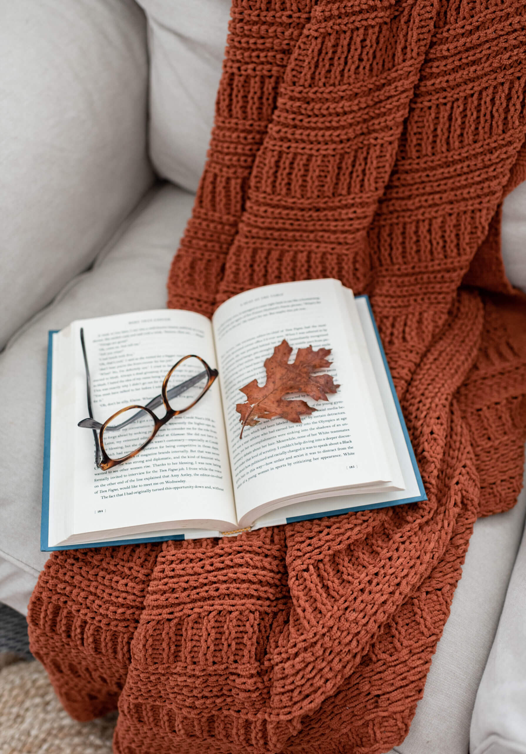 Orange blanket with open book, fall leaf, and reading glasses
